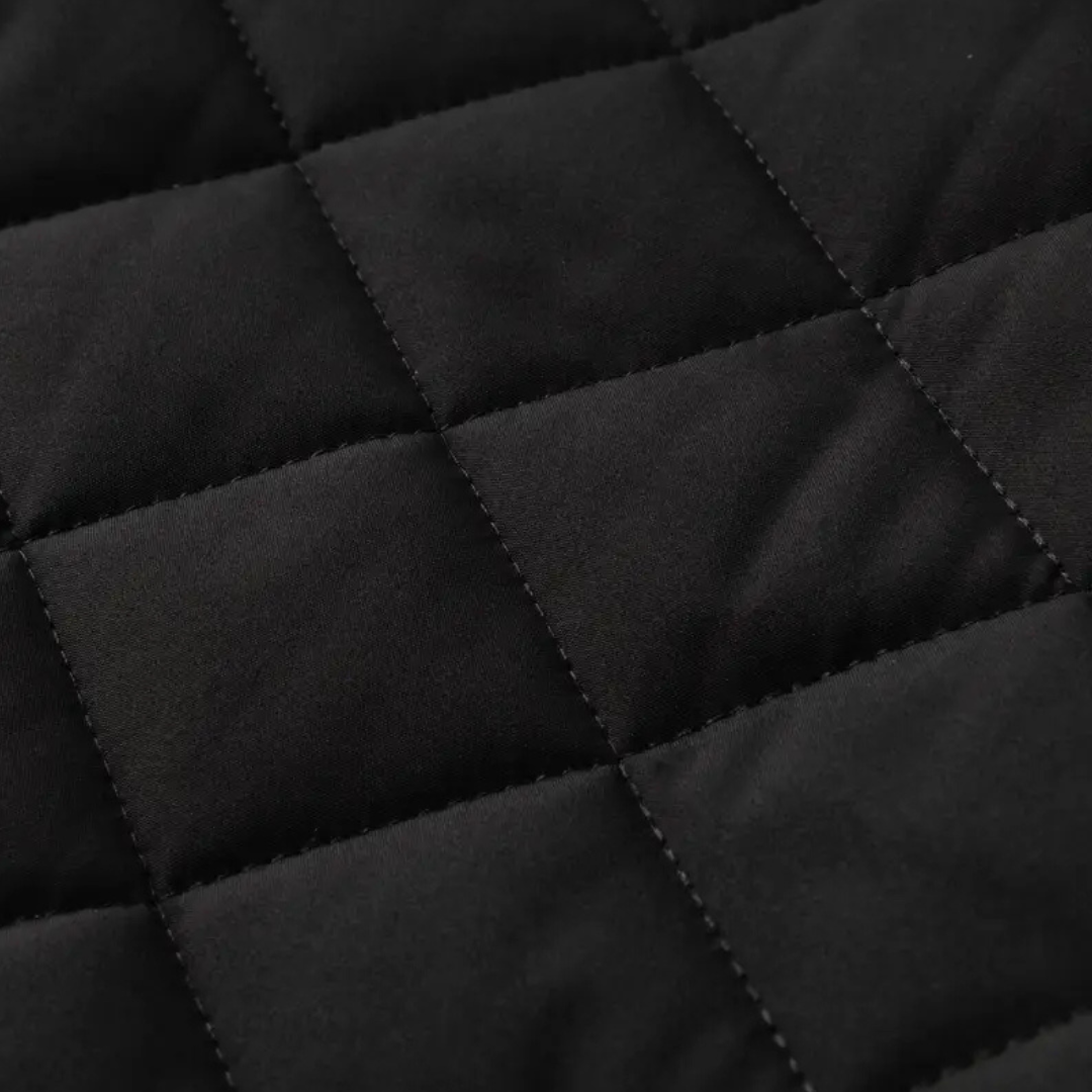 Detal rombowego pikowania na czarnym, matowym materiale z widocznym szwem krzyżowym.