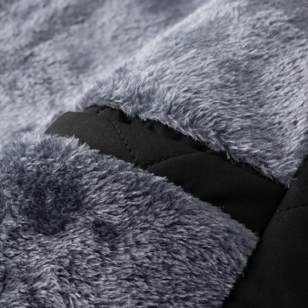 Zbliżenie na futerkową podszewkę kurtki z miękkiego, szarego materiału oraz wewnętrzną kieszeń obszytą czarną tkaniną.