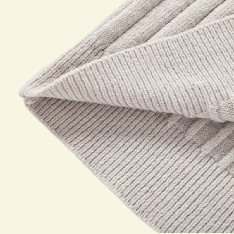 Zbliżenie na prążkowaną dzianinę kremowego swetra, miękka faktura i elastyczne wykończenie.