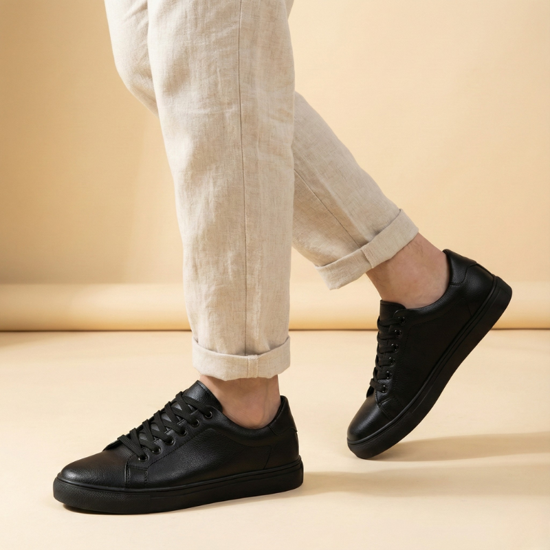 Czarne niskie sneakersy męskie noszone przez modela, widok z boku podczas chodzenia, zestawione z jasnymi spodniami.