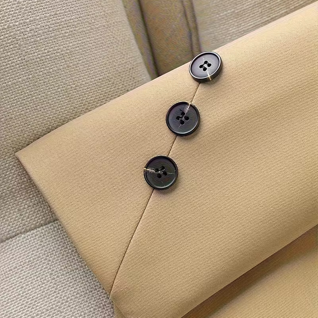 Zbliżenie na rękaw beżowej marynarki z trzema czarnymi guzikami.