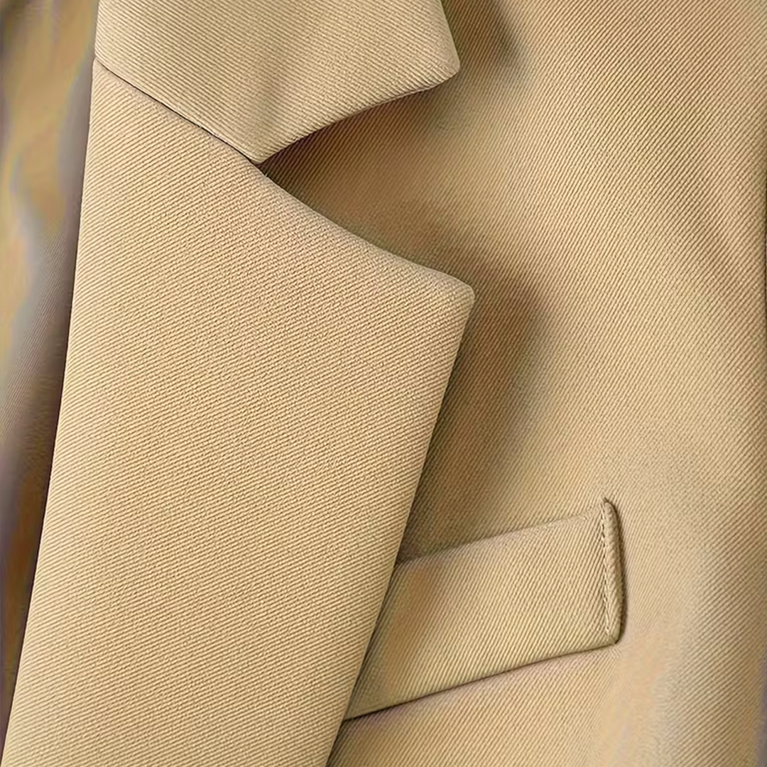 Zbliżenie na klapę beżowej marynarki oraz strukturę tkaniny.