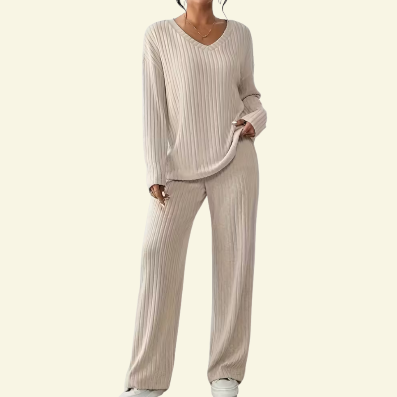 Modelka w kremowym prążkowanym komplecie, pełne ujęcie sylwetki z przodu. Luźna bluzka z dekoltem V i proste spodnie z miękkiej dzianiny.