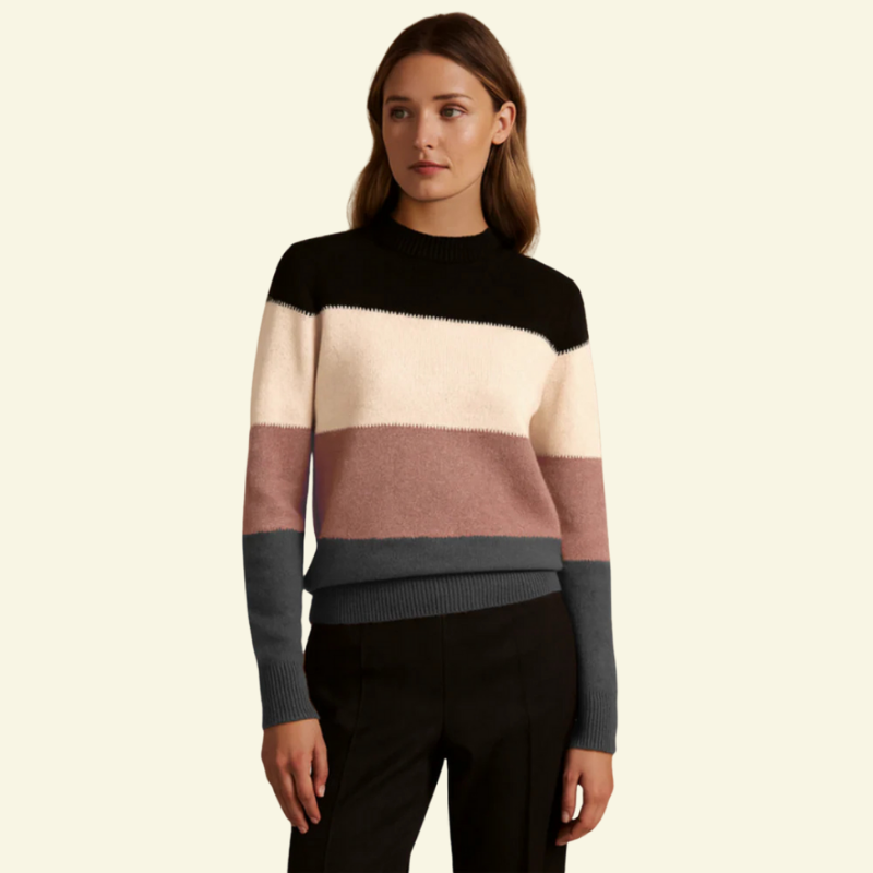 Modelka w swetrze color-block w pudrowym różu; półgolf, luźny krój i wyraźne poziome pasy.