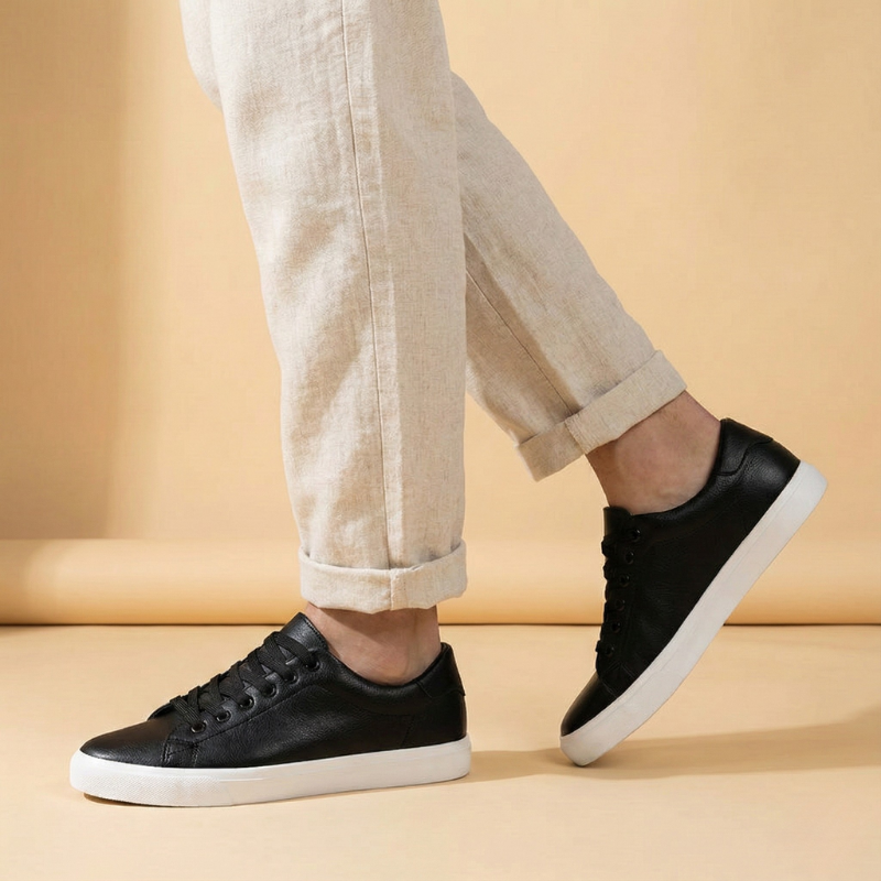 Czarne niskie sneakersy męskie noszone na stopach modela, widok z boku, zestawione z jasnymi spodniami w codziennej stylizacji.