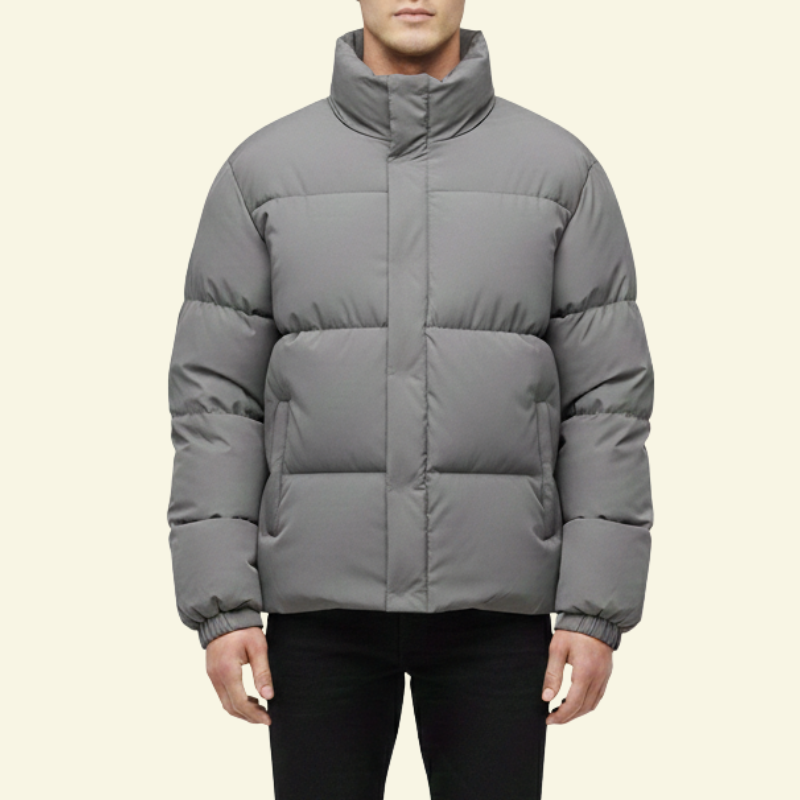 Mężczyzna prezentujący srebrnoszarą kurtkę puchową z przodu. Kurtka o regularnym kroju, z wysokim kołnierzem i subtelnym połyskiem tkaniny, tworząca zimowy, codzienny look.